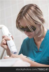 Close-up shot of woman in safety glasses working with laser during facial treatment in cosmetology clinic