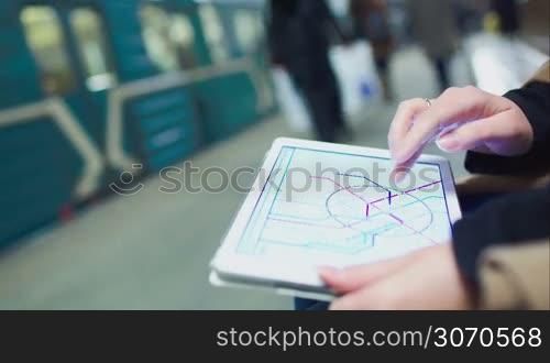 Close-up shot of woman looking at metro map on pad while she waiting at undeground station