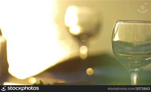 Close-up shot of woman pouring a water or wine from glass bottle and taking wineglass to have a drink in bright evening sunshine