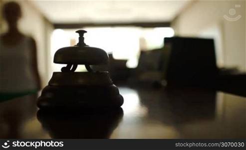 Close-up shot of woman ringing reception bell on counter desk in hotel