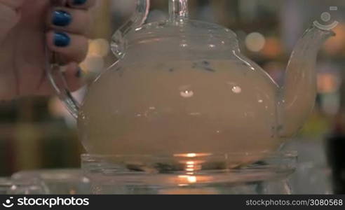 Close-up shot of woman taking a glass pot from candle heating and pouring masala tea into a glass cup