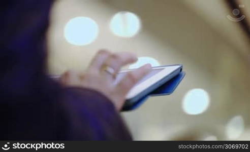 Close-up shot of woman typing on her tablet while riding on escalator. Defocused lights in background