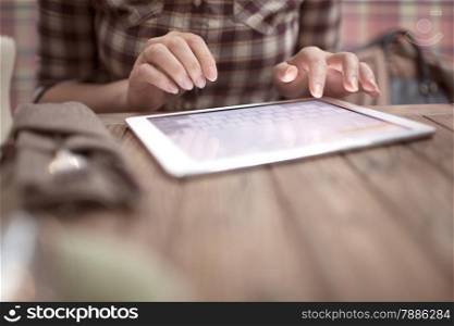 Close-up shot of woman typing on tablet computer sitting at the wooden in cafe