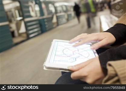 Close-up shot of woman using tablet computer in subway. She looking at underground map on pad screen, blurred station with train in background