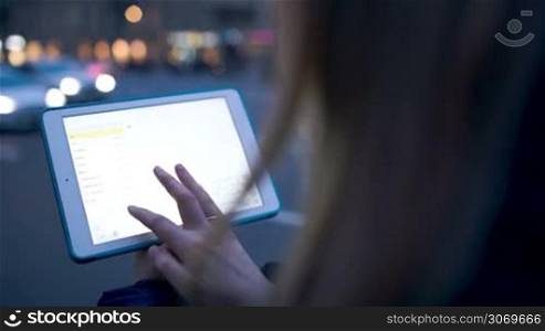 Close-up shot of woman using touch pad outdoor in the city in the evening. Bright shining pad screen in focus
