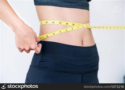 Close up shot of woman with slim body measuring her waistline and torso. Healthy nutrition and weight losing concept.