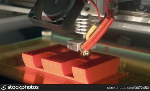 Close-up shot of working 3D printer making letter E. It using technology of laying down successive layers under computer control. Object of any shape can be made from 3D model or other electronic data source
