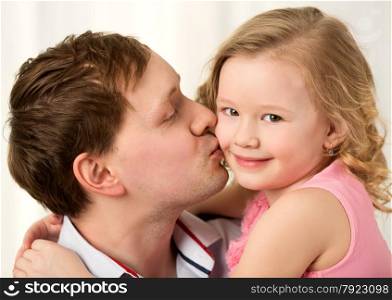 Close-up shot of young father kissing little smiling daughter. Sincere parents love. Daddy kissing beautiful little daughter