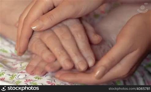 Close-up shot of young female hands holding and stroking hands of senior woman. Taking care of aged people concept