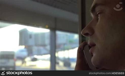 Close-up shot of young man talking on the mobile phone. Window with airport area view in background