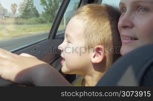 Close-up shot of young mother and little son looking at the city through the window of a moving car. Interesting ride with lots to see