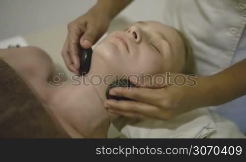 Close-up shot of young woman enjoying spa neck massage with stones. Therapy at beauty spa