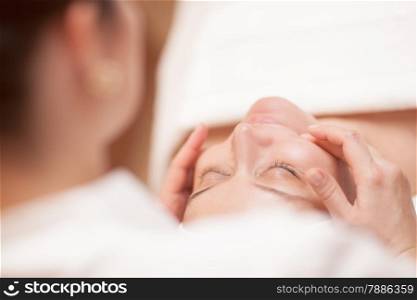 Close-up shot of young woman getting professional facial massage at beauty treatment salon. Focus on a woman
