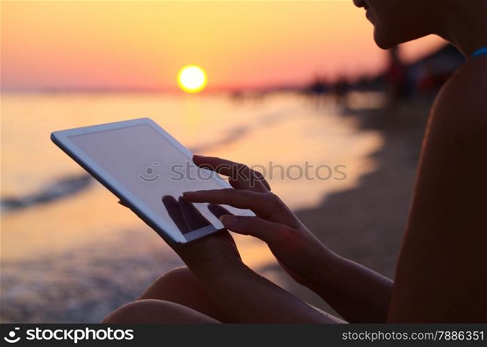 Close-up shot ofwoman working with tablet computer on sunset and sea background