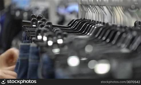 Close-up shot with changing focus of female hands looking over jeans hanging on the racks in the store