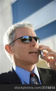 Close up side view of prime adult Caucasian man in suit talking on cellphone in urban setting.