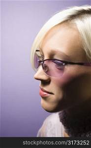 Close-up side view portrait of young adult Caucasian woman on purple background wearing sunglasses.