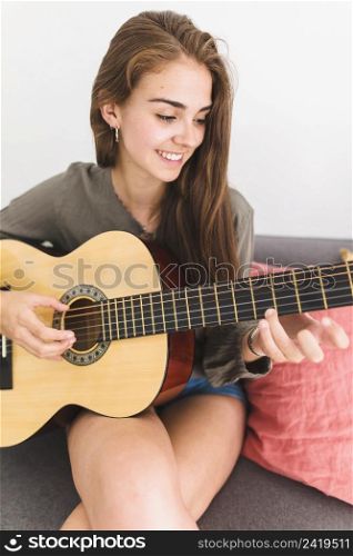 close up smiling teenage girl playing guitar home