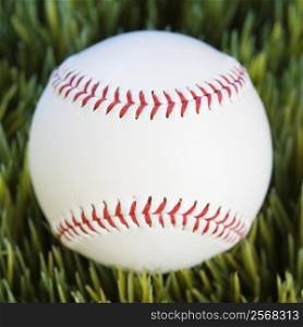 Close-up studio shot of baseball resting in grass.