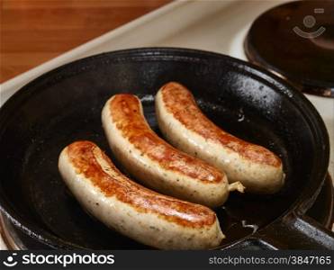 Close up, three sausages fried in cast iron pan