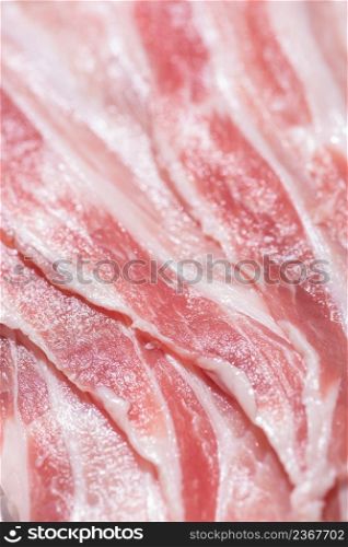 Close up top view pack bacon, pieces raw meat of fresh red pork with white fat slices are sliced into thin strips stacked on top of each other. Closeup pack fresh bacon pork slices