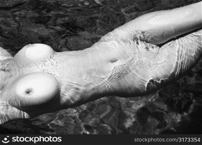 Close up torso of young adult nude Caucasian woman floating in water in Maui.