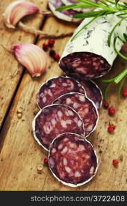 Close-up traditional sliced meat sausage salami on wooden board with head of garlic and green herbs