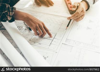 Close up two architect hands holding pencil and pointing on building blueprints in office room.