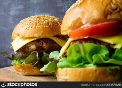 close up two fresh tasty homemade hamburgers with fresh vegetables, lettuce, tomato, cheese beside sliced tomatoes on a cutting board. Free space for text