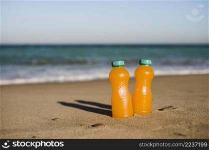 close up two orange juice bottles near seashore
