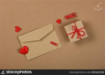 Close up Valentine gift box with red twine bow and card greeting envelope with wooden clothespins and hearts over brown paper background, flat lay, elevated top view, directly above