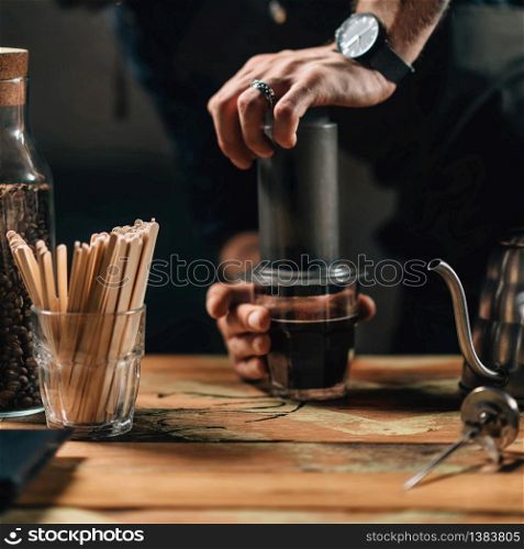 Close up vertical image of barista making air press coffee. Barista with tattooed arms wearing dark uniform.