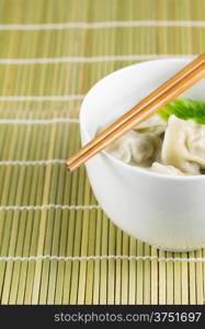 Close up vertical photo of freshly made wonton with chopsticks on top of white bowl