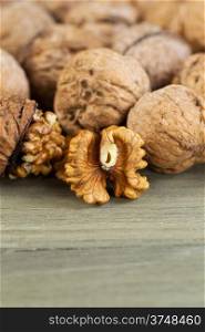 Close up vertical photo of unshelled half of walnuts lying on faded wood with additional nuts both shelled and unshelled in background