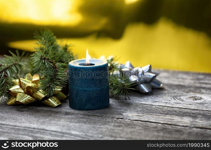 Close up view of a burning blue candle with a glowing golden background plus fir branches and shiny gift bows for a Merry Christmas or Happy New Year theme