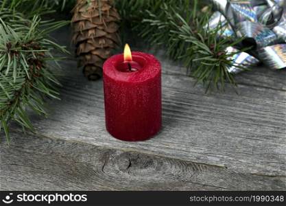 Close up view of a glowing red candle with fir branches and shiny silver gift bows on aged wooden planks for a Merry Christmas or Happy New Year