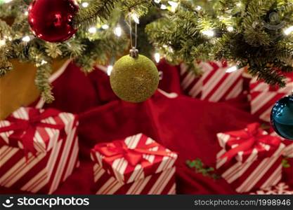 Close up view of a hanging golden ball ornament with lighten fir tree and presents in background for a Merry Christmas or Happy New Year concept