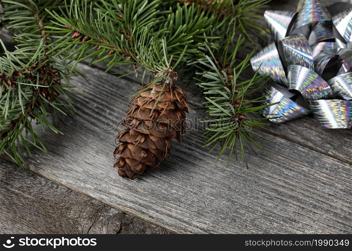 Close up view of a single pine cone with fir branches and shiny silver gift bows on aged wooden planks for a Merry Christmas or Happy New Year