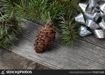 Close up view of a single pine cone with fir branches and shiny silver gift bows on aged wooden planks for a Merry Christmas or Happy New Year