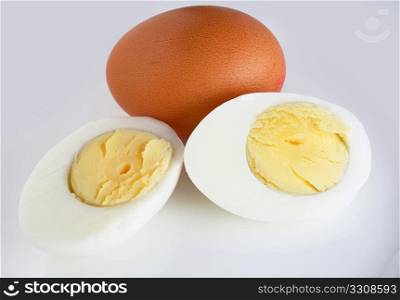Close-up view of a sliced boiled egg and a fresh brown egg against a plain backgroun