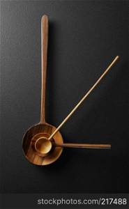 close-up view of a wooden spoons with clock hands. Top view of black alarm clock with wooden spoons