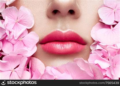 Close up view of beautiful woman lips with pink lipstick in flowers. Cosmetology, drugstore or fashion makeup concept. Models face in decorated with flowers