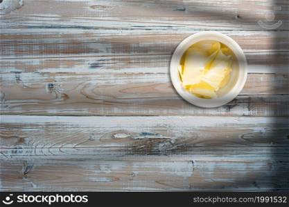 Close up view of cheese slices on ceramic bowl over wooden table.
