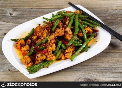 Close up view of crispy fried chicken pieces with green beans and Chile peppers on rustic wood setting.