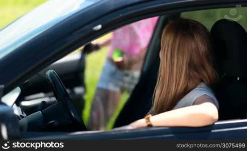 Close up view of cute blonde woman is waiting in the car for her friend. Smiling brunette joins her girlfriend with warm greetings