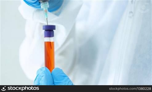 Close up view of doctor in bioprotective suit and blue gloves taking a blood sample in a test tube with a syringe on white background. Close up view of doctor in bioprotective suit and blue gloves taking a sample from a test tube with a syringe on white background