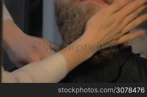 Close up view of female barber taking cares of lush beard of white man