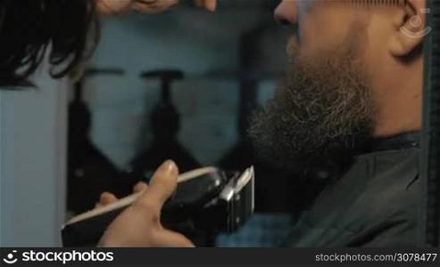 Close up view of female barber taking cares of lush beard of white old man. Barber combing and trimming beard