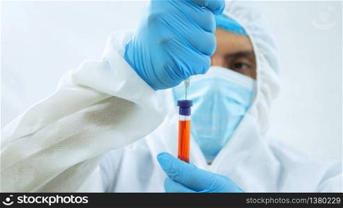 Close up view of latin doctor in bioprotective suit, face mask and blue gloves taking a blood sample in a test tube with a syringe on white background. Close up view of latin doctor in bioprotective suit, face mask and blue gloves taking a sample from a test tube with a syringe on white background