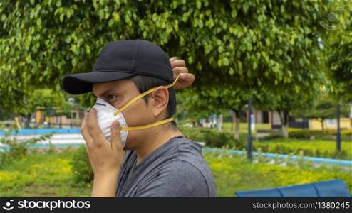 Close up view of latin man on the street putting on a white face mask using both hands. Latin man on the street putting on a white face mask using both hands